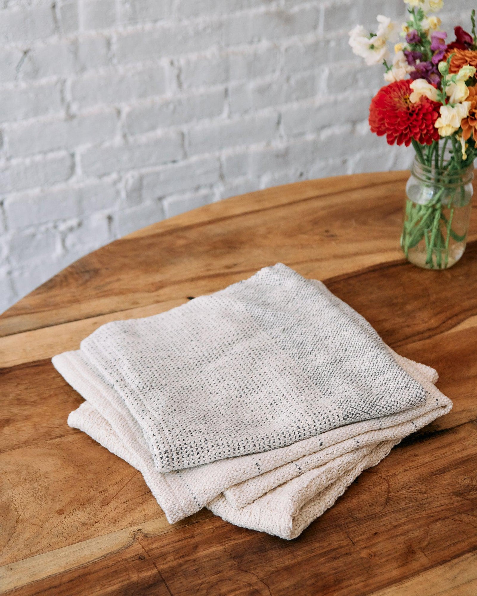 Forest Walk - Set of Three Patterns showing folded minimalist textured handwovens on wooden table with flowers.