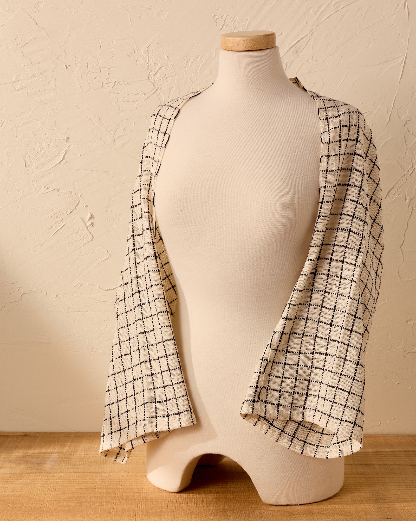 Mannequin wearing a black and white handwoven shawl against a beige wall.