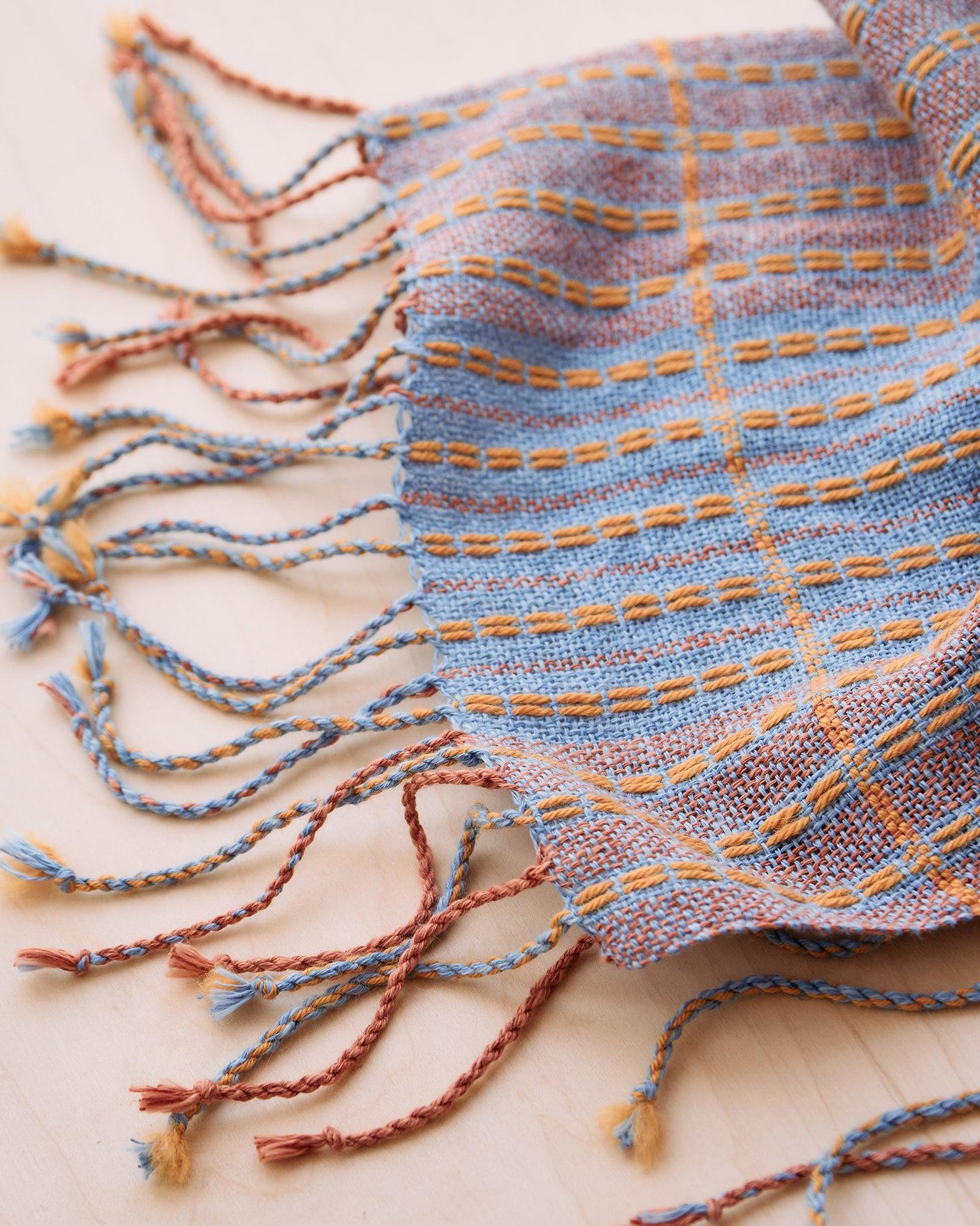 Chroma - Set of Three Patterns showing woven blue and orange fabric with braided fringe on light wood surface.