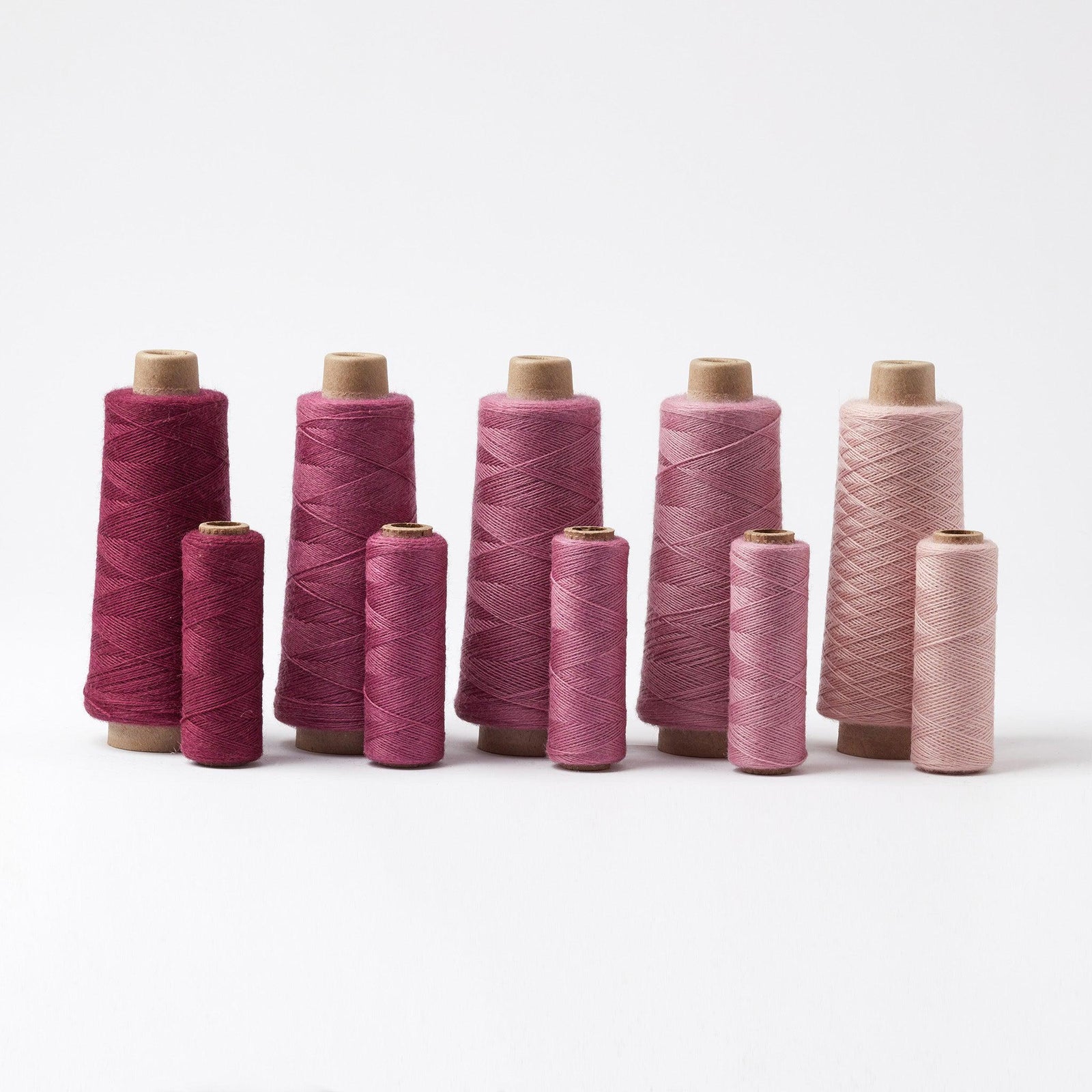 Array Wool Yarn ~ Burgundy cones and tubes in various shades from deep burgundy to soft pink arranged in a row on white background