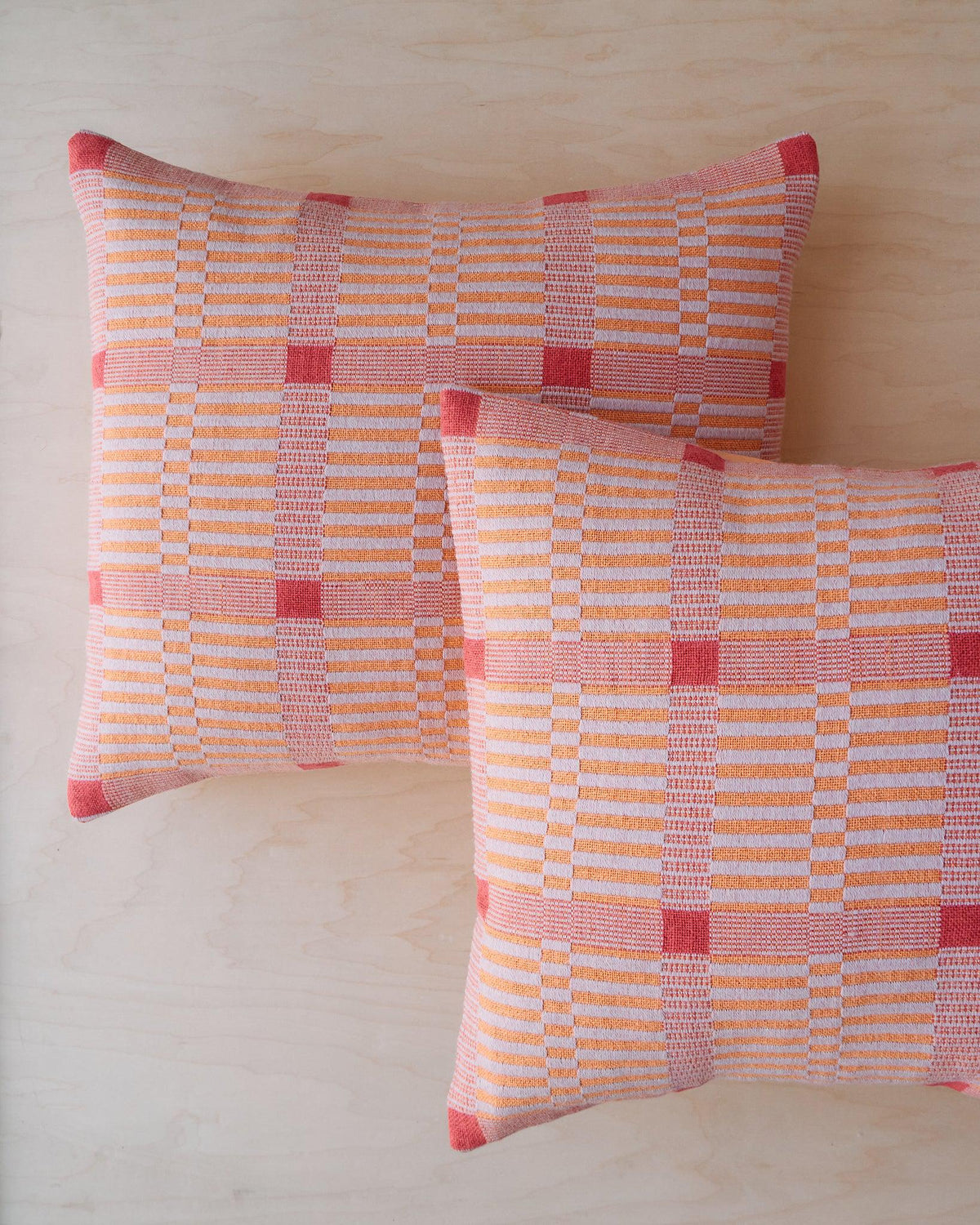 Chroma - Set of Three Patterns featuring two woven pillows in orange, pink, and red plaid design on wood surface.