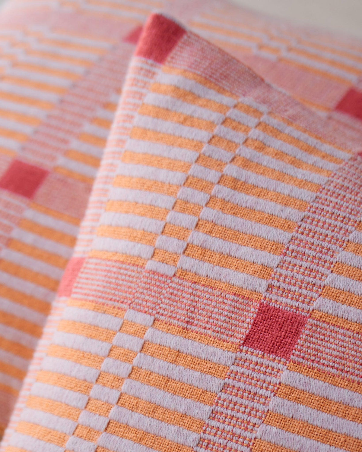 Close-up of woven fabric in pink, orange, and red tones from Chroma - Set of Three Patterns.