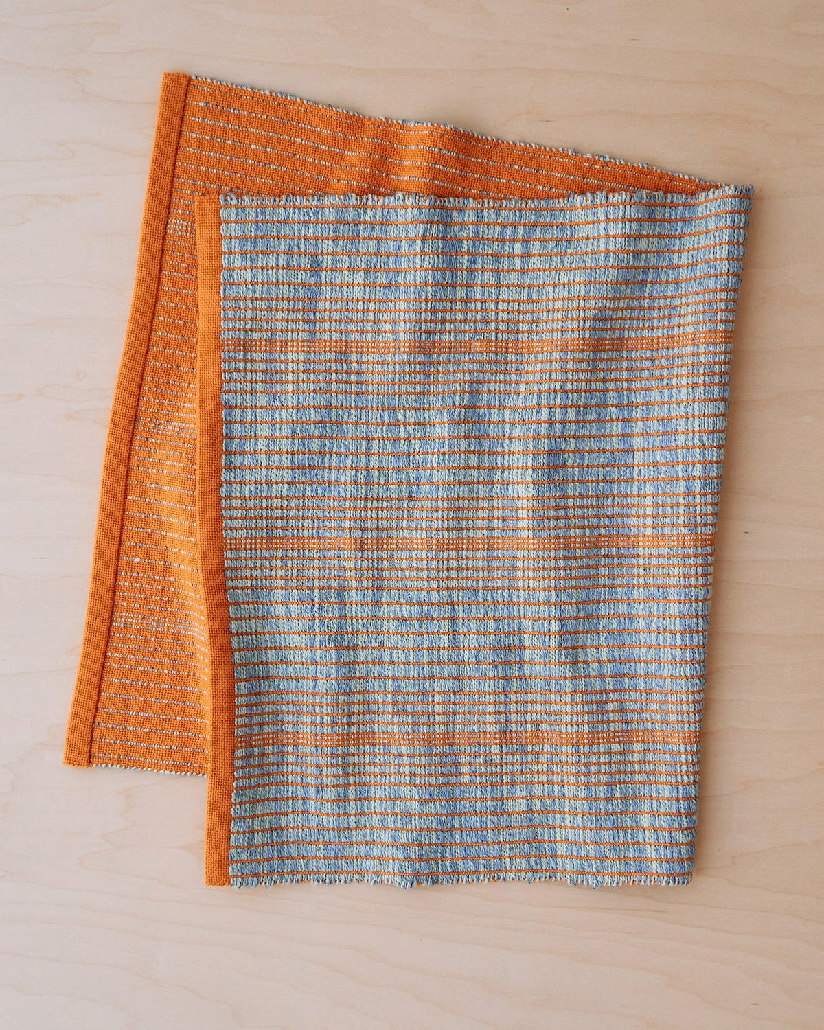 Chroma - Set of Three Patterns showing two woven fabrics in orange and blue striped design on a light wood surface.