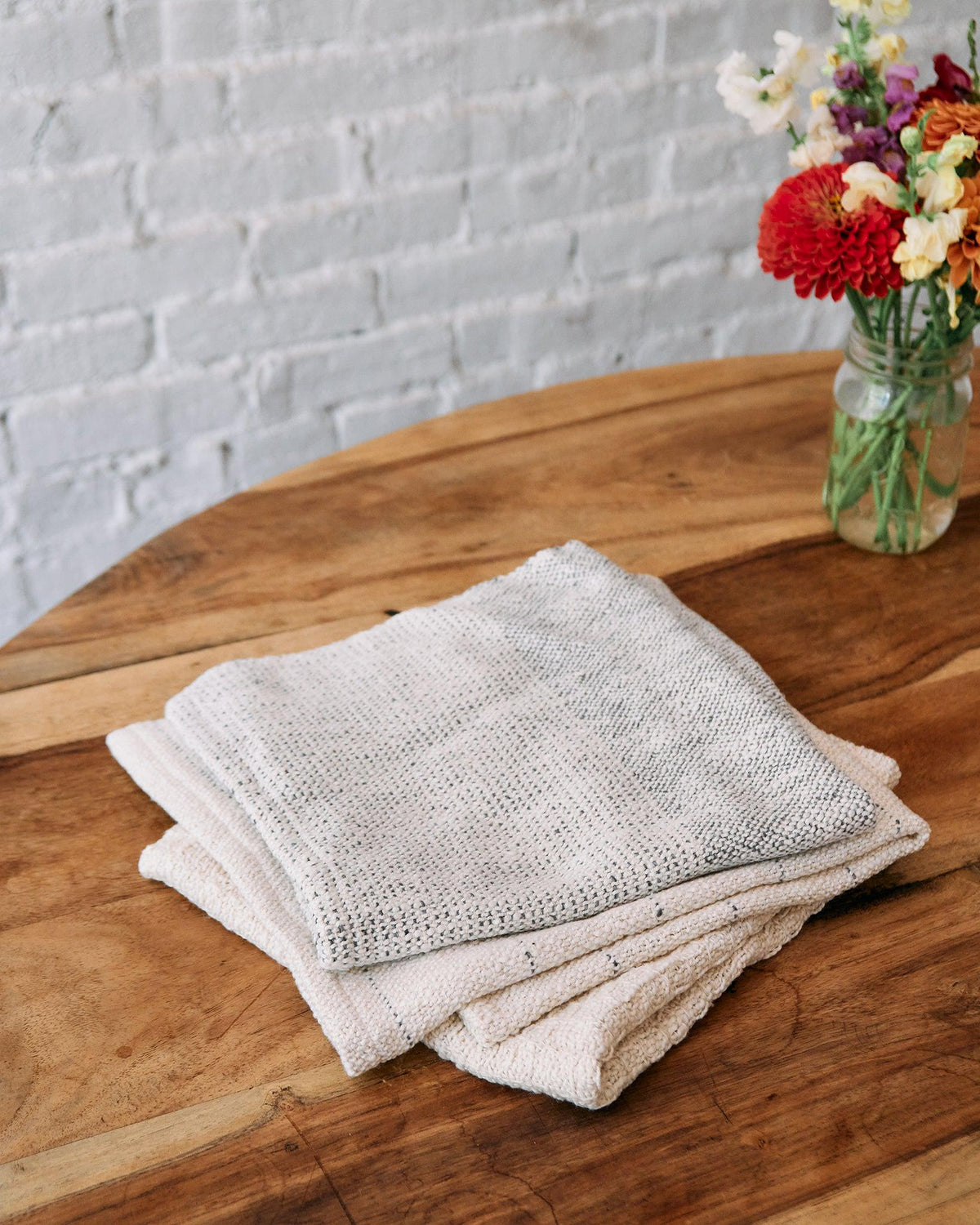 Forest Walk - Set of Three Patterns showing folded minimalist textured handwovens on wooden table with flowers.