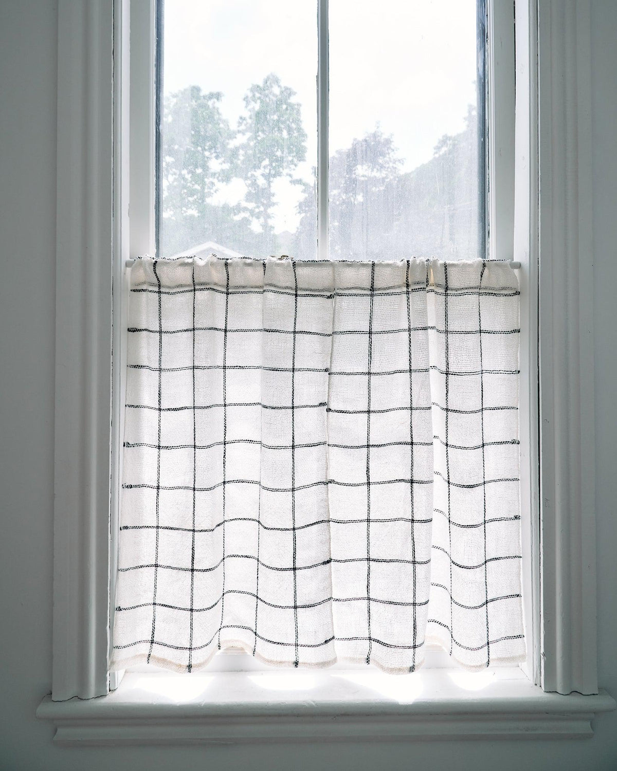 Forest Walk - Set of Three Patterns showing minimalist handwoven white curtain with black grid lines on window.