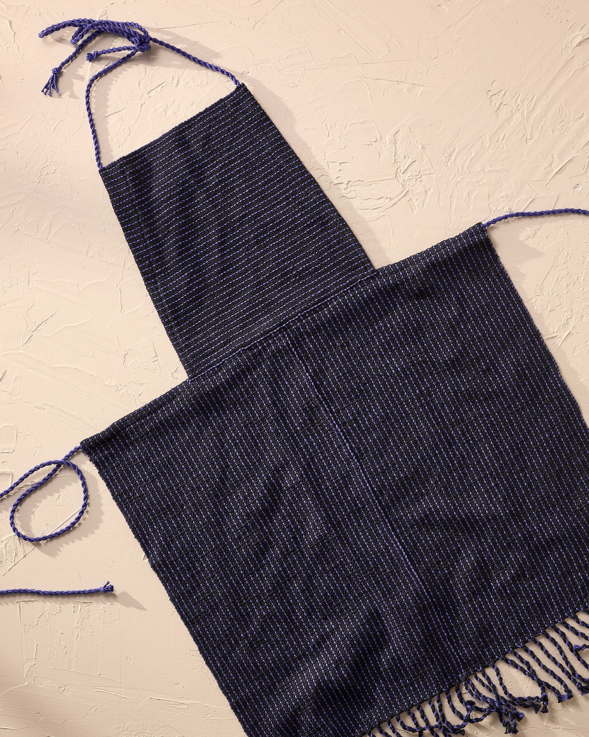 Navy blue woven apron with thin straps on a beige textured background