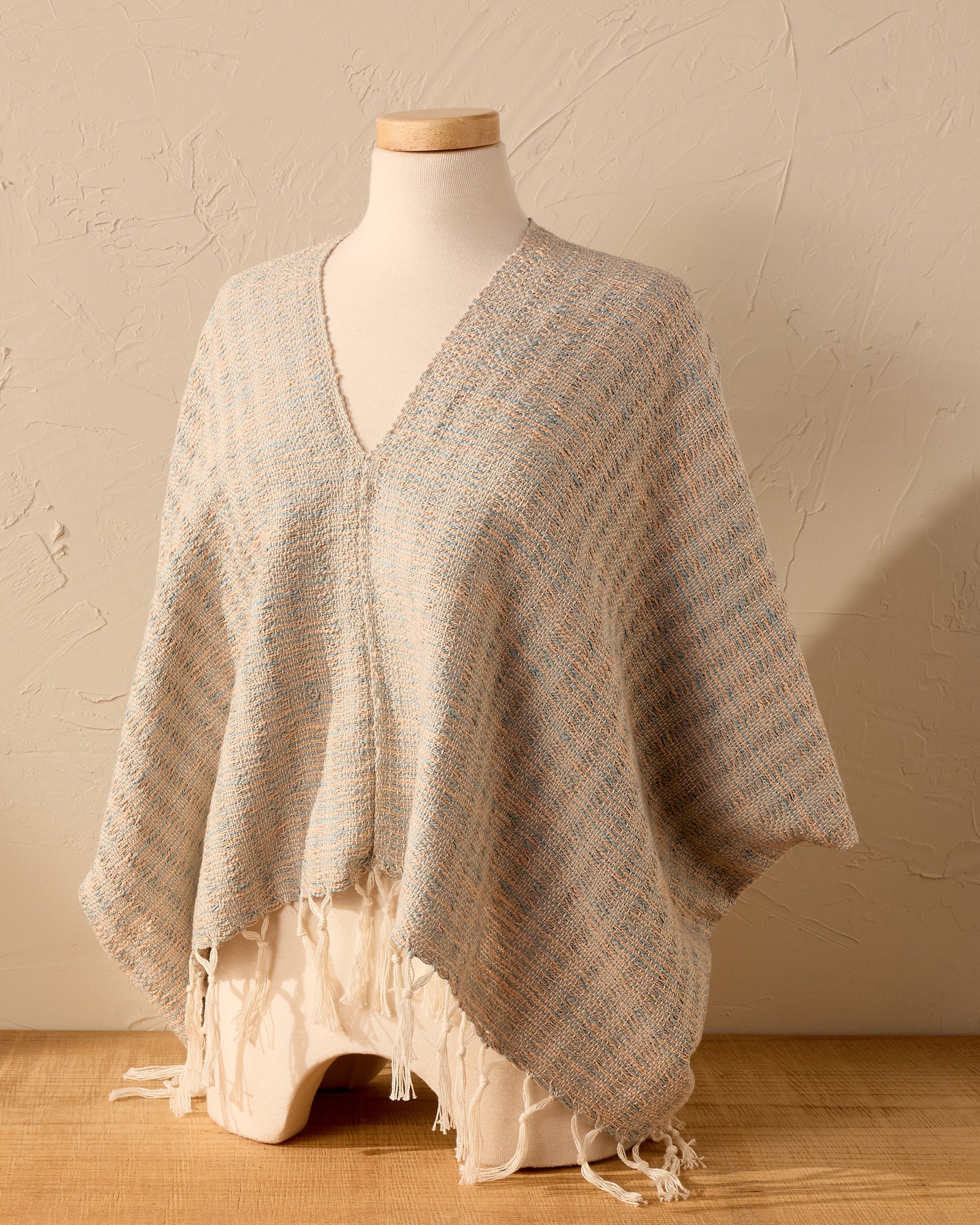 Textured woven poncho on a mannequin against a beige wall