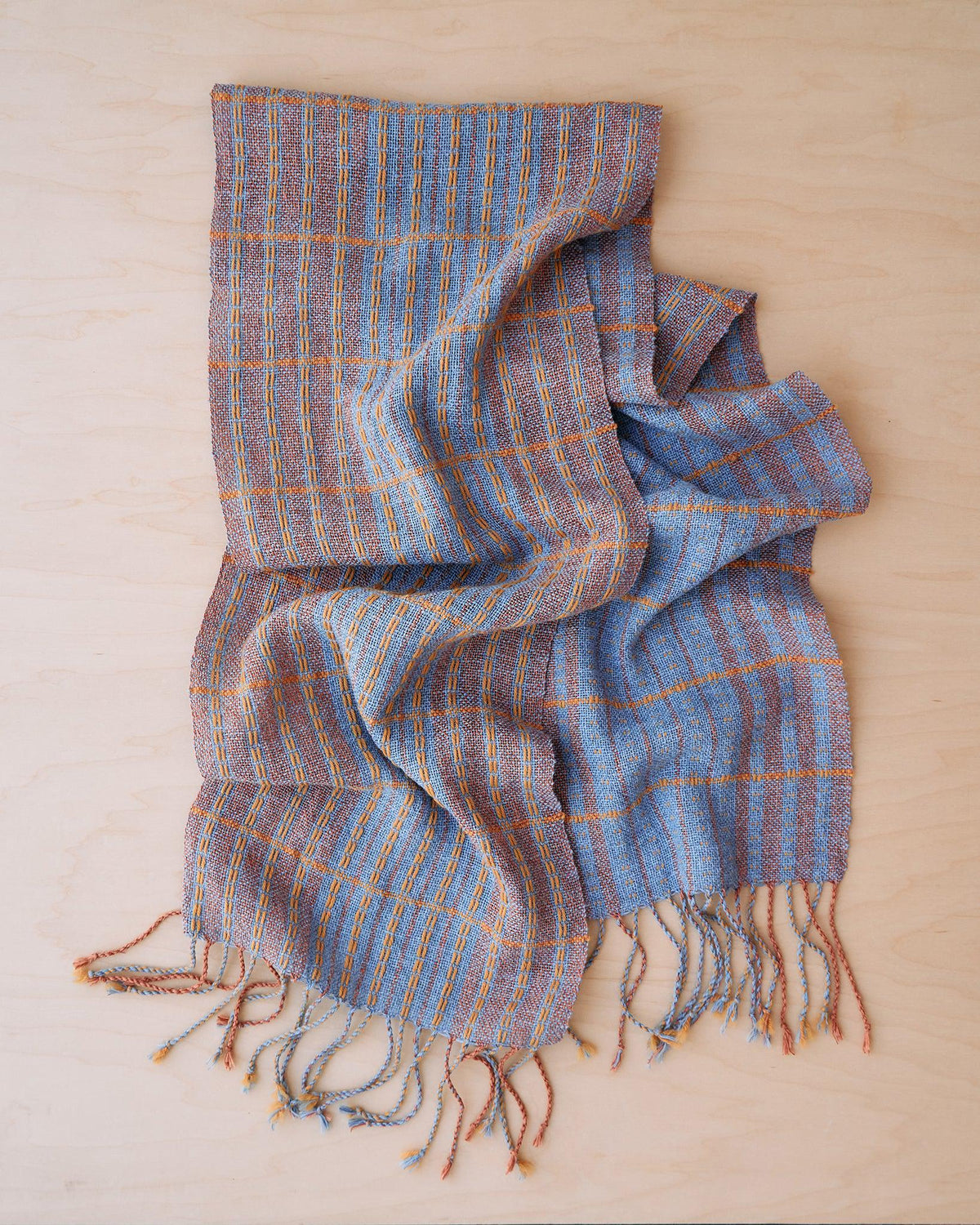 Chroma - Set of Three Patterns woven scarf showing colorful stripes and fringe on a wooden surface.