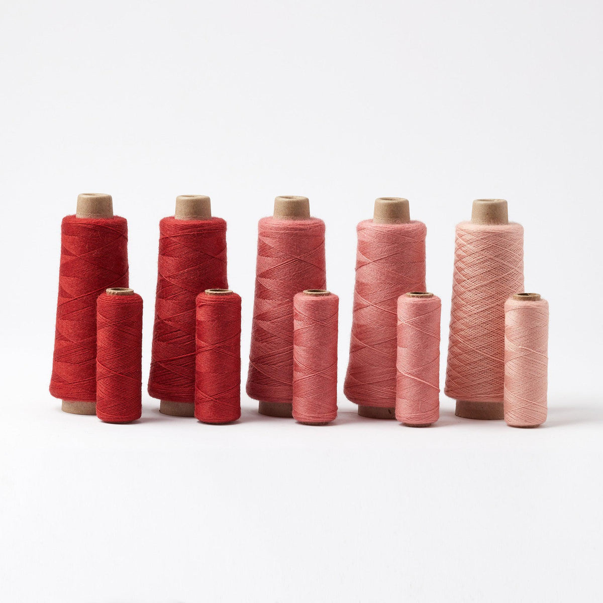 Array Wool Yarn ~ Cayenne in varying shades of red and pink, displayed in different sized cones and tubes.