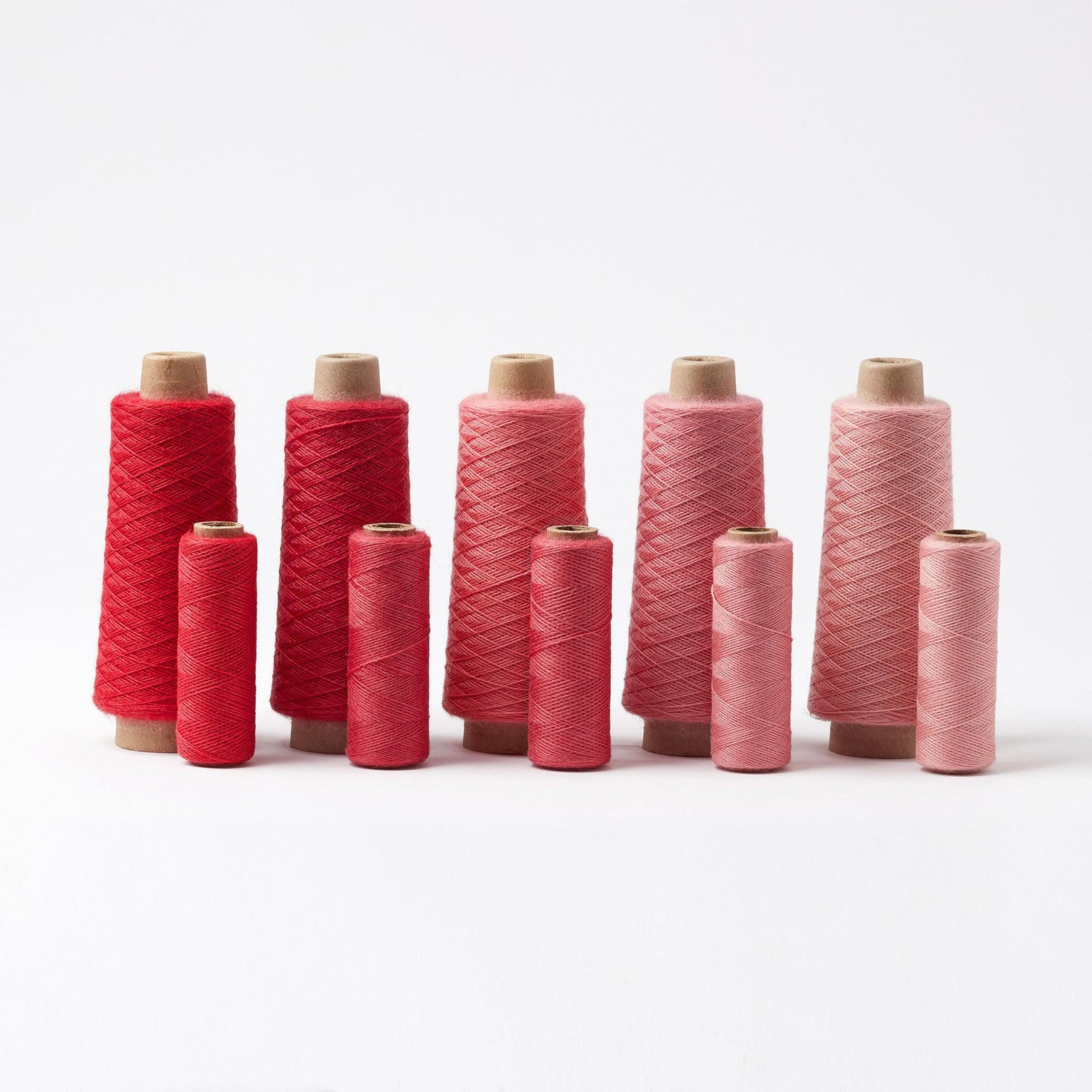 Array Wool Yarn ~ Cherry in various shades from deep red to light pink, displayed on cones and tubes.