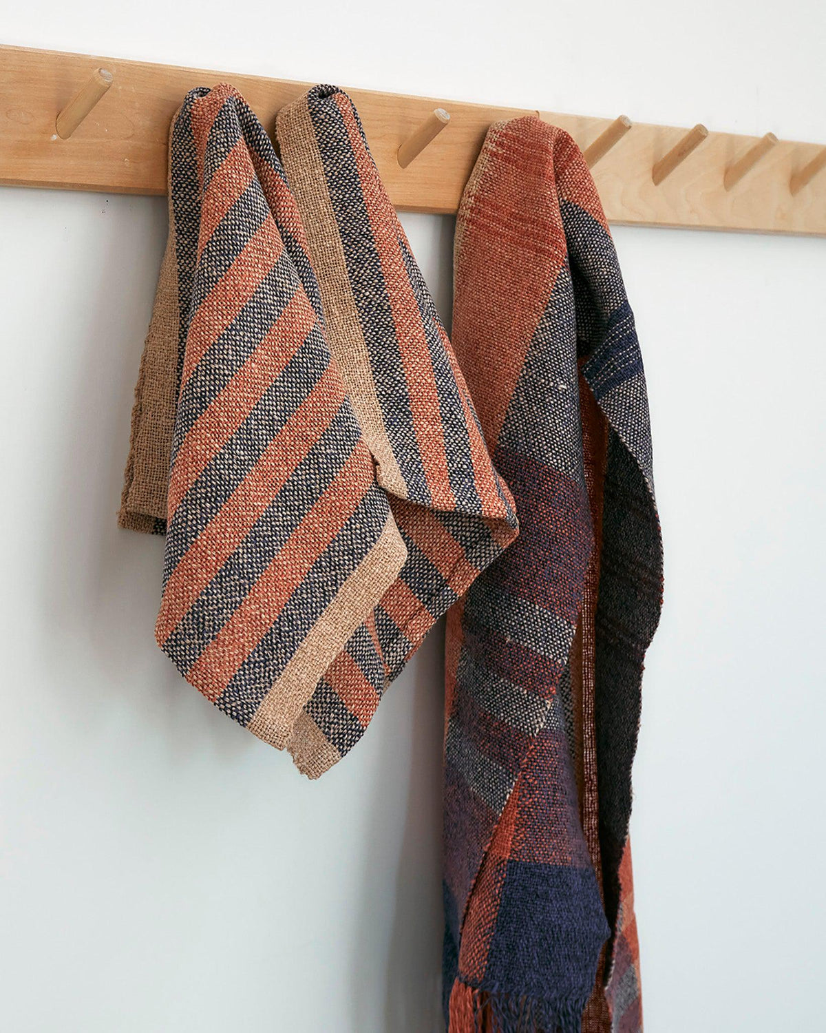 Duet Favorites - Set of Two Patterns featuring woven striped Citrus Towels and Minimalist Scarf in warm tones hanging on hooks.